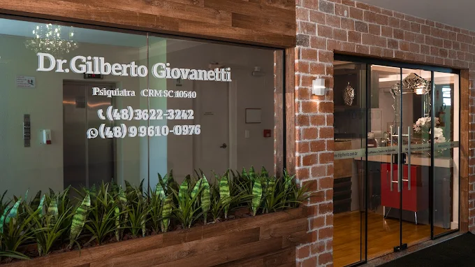 Entrada do consultório, com o nome Dr. Gilberto Giovanetti, Psiquiatra CRM SC 10540 e os telefones (48) 3622-3242 e (48) 99610-0976 aplicados na vidraça.